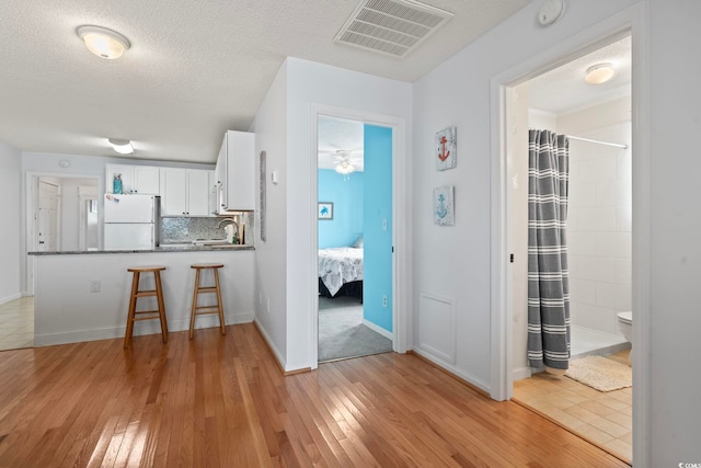 kitchen with tasteful backsplash, visible vents, freestanding refrigerator, light wood-type flooring, and white cabinetry