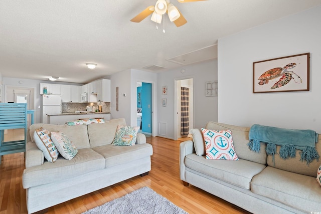 living room featuring ceiling fan, a textured ceiling, baseboards, light wood-type flooring, and attic access