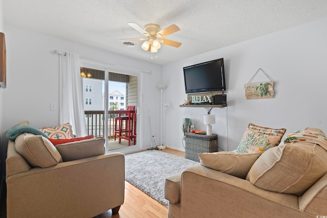 living room with ceiling fan, a textured ceiling, visible vents, and wood finished floors