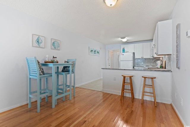 kitchen with tasteful backsplash, freestanding refrigerator, white cabinetry, a sink, and a peninsula