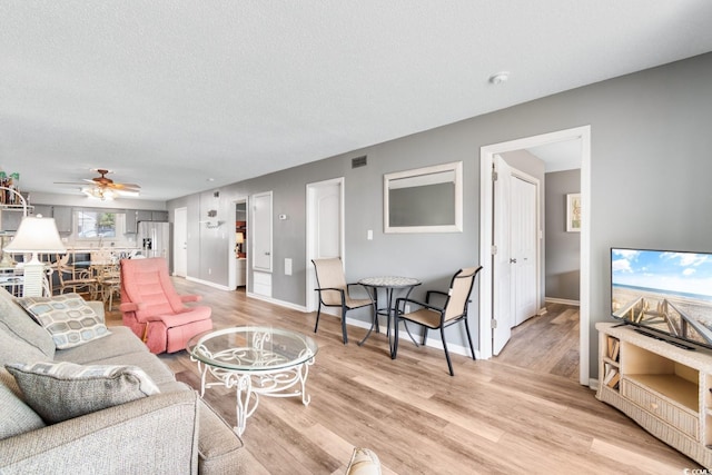 3308 S Ocean Blvd Unit 2-A, North Myrtle Beach, SC 29582 - living room with light wood finished floors, baseboards, ceiling fan, and a textured ceiling