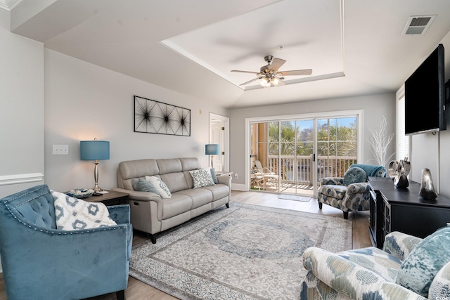 living area featuring a ceiling fan, a tray ceiling, visible vents, and wood finished floors