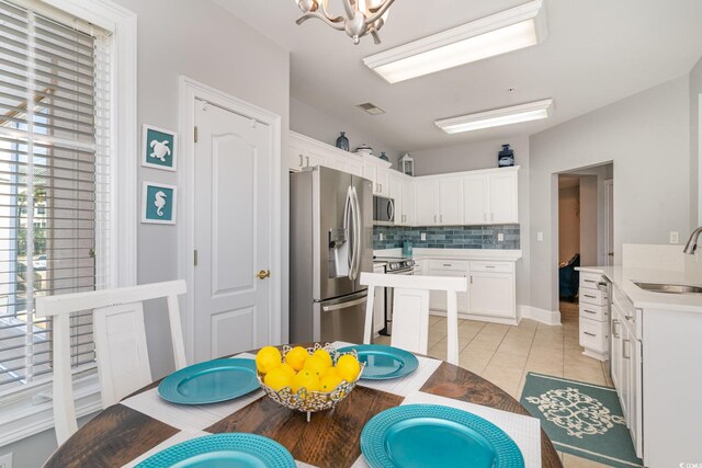 kitchen featuring light tile patterned floors, tasteful backsplash, white cabinets, appliances with stainless steel finishes, and a sink