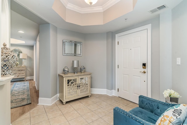 foyer featuring visible vents, a raised ceiling, crown molding, and light tile patterned flooring