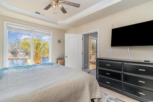 bedroom with light wood-type flooring, a tray ceiling, crown molding, and ensuite bathroom