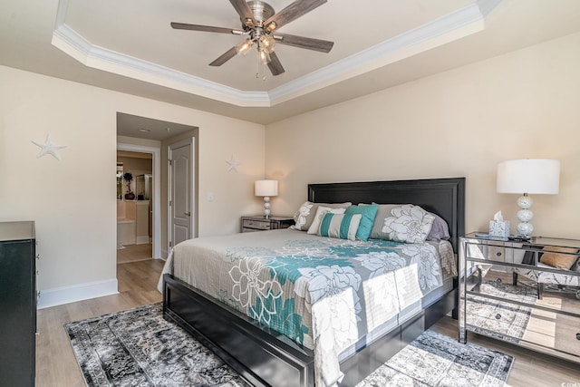 bedroom with baseboards, crown molding, a tray ceiling, and wood finished floors