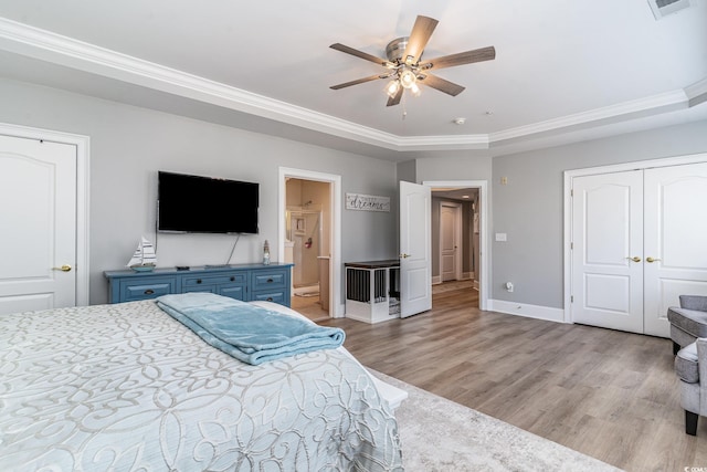 bedroom featuring wood finished floors, a ceiling fan, baseboards, a tray ceiling, and ensuite bath