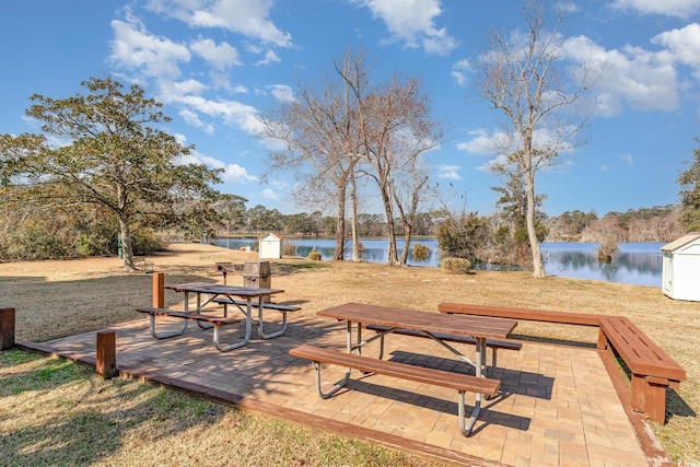 view of property's community with outdoor dining area, a water view, an outdoor structure, and a storage shed