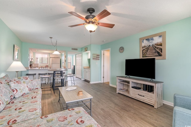 living room featuring a textured ceiling, wood finished floors, visible vents, and baseboards