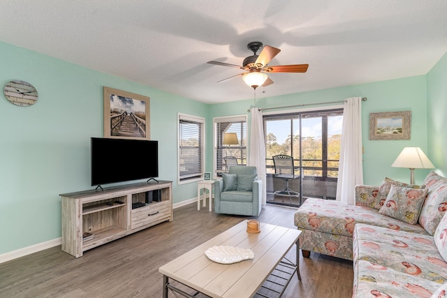 living room featuring ceiling fan, a textured ceiling, baseboards, and wood finished floors