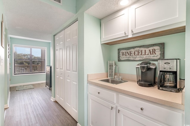 bar featuring a textured ceiling, wood finished floors, a sink, and baseboards