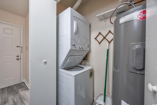 washroom featuring stacked washer / drying machine, laundry area, water heater, and wood finished floors