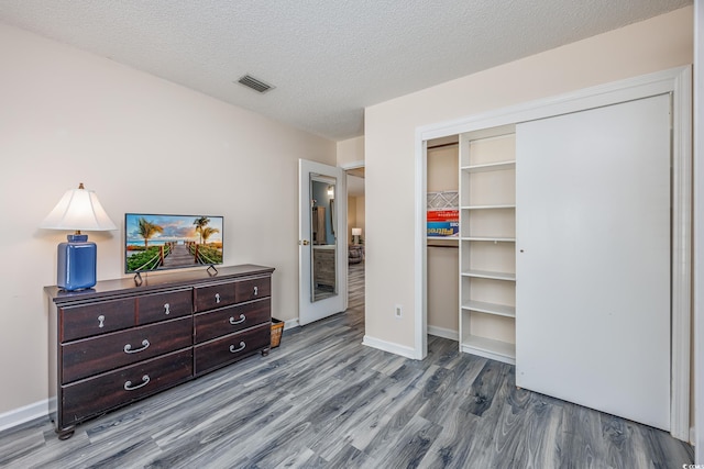 bedroom featuring a textured ceiling, wood finished floors, visible vents, baseboards, and a closet