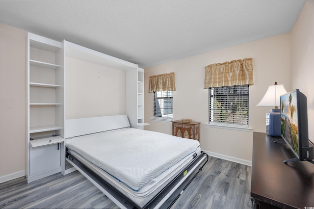 bedroom with a textured ceiling, baseboards, and wood finished floors