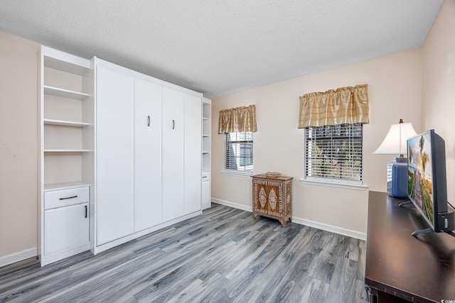 unfurnished bedroom with a textured ceiling, baseboards, and wood finished floors