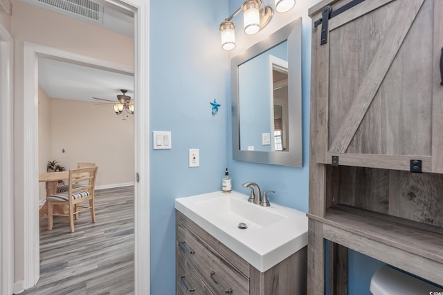 half bath featuring baseboards, visible vents, a ceiling fan, wood finished floors, and vanity