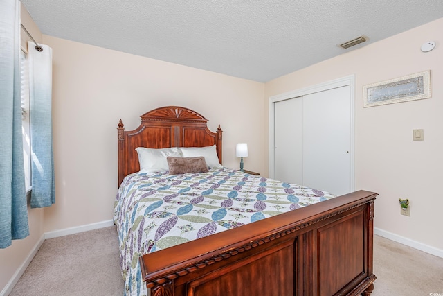 bedroom featuring baseboards, visible vents, light colored carpet, a textured ceiling, and a closet