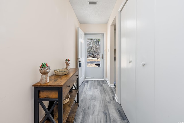 entryway featuring baseboards, visible vents, a textured ceiling, and wood finished floors