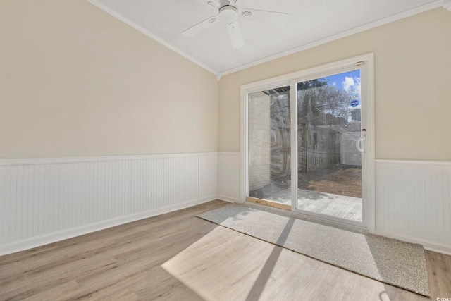 unfurnished room with lofted ceiling, wood finished floors, a ceiling fan, wainscoting, and crown molding