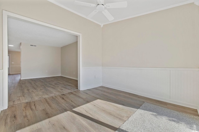 spare room with a wainscoted wall, wood finished floors, visible vents, a ceiling fan, and ornamental molding