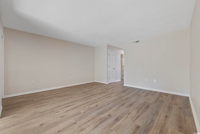 empty room with baseboards, a textured ceiling, visible vents, and wood finished floors