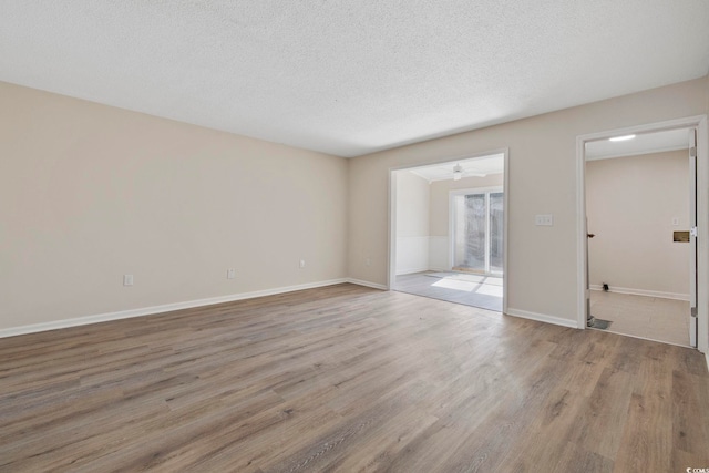 spare room with light wood-style floors, a textured ceiling, baseboards, and a ceiling fan