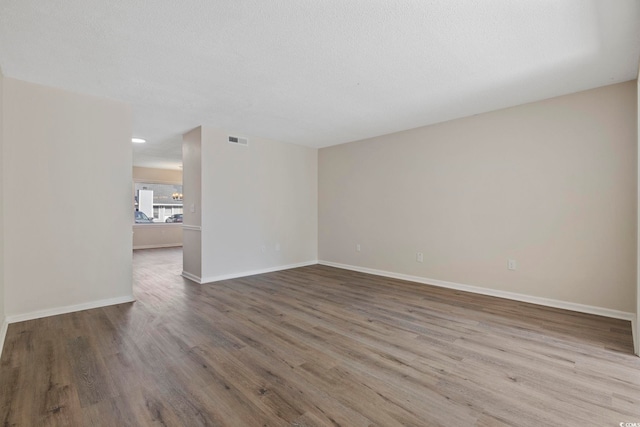 unfurnished room featuring visible vents, a textured ceiling, baseboards, and wood finished floors