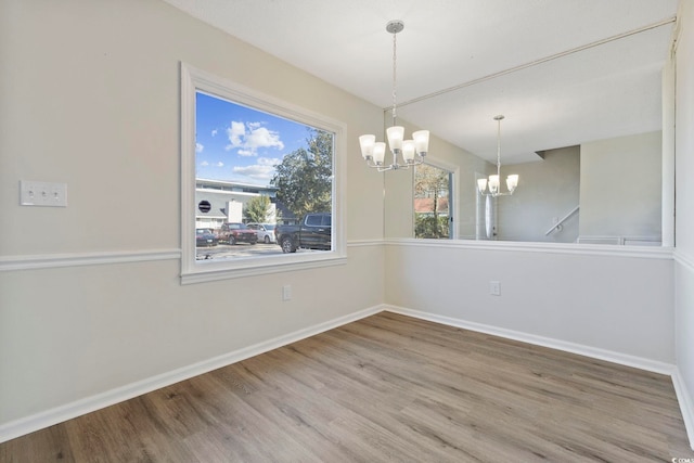 unfurnished room featuring baseboards, wood finished floors, and an inviting chandelier