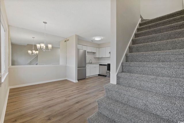 staircase with a chandelier, wood finished floors, and baseboards