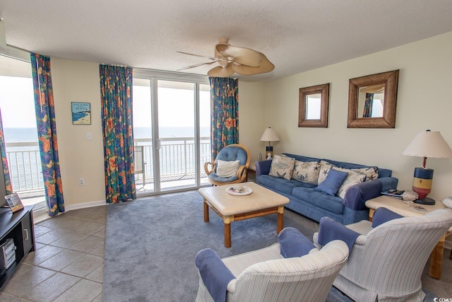 living area featuring baseboards, a ceiling fan, a water view, tile patterned flooring, and a textured ceiling