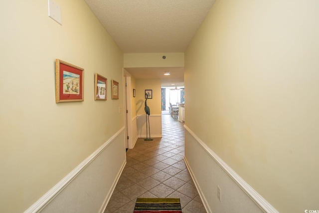 hallway featuring a textured ceiling, tile patterned flooring, and baseboards