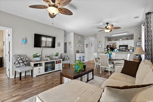 living area with arched walkways, light wood finished floors, visible vents, ceiling fan, and baseboards