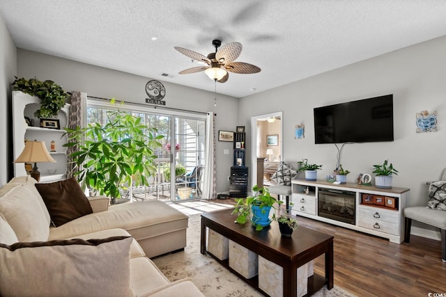 living area with a textured ceiling, wood finished floors, visible vents, and a ceiling fan