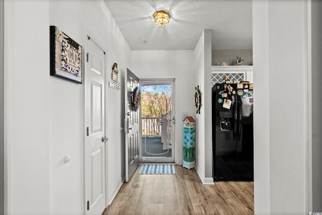 doorway to outside featuring a textured ceiling, light wood-style flooring, and baseboards