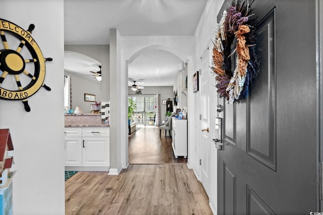 entrance foyer with arched walkways, a textured ceiling, light wood-type flooring, and a ceiling fan