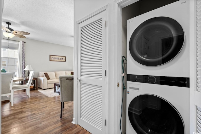 laundry room featuring stacked washer and dryer, ceiling fan, a textured ceiling, wood finished floors, and laundry area