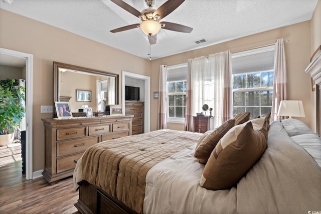 bedroom with ceiling fan, a textured ceiling, visible vents, and wood finished floors