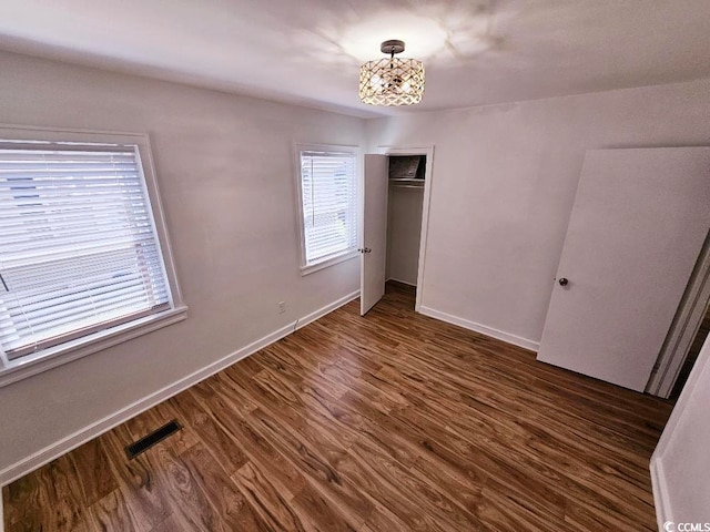 unfurnished bedroom featuring a closet, dark wood finished floors, visible vents, and baseboards