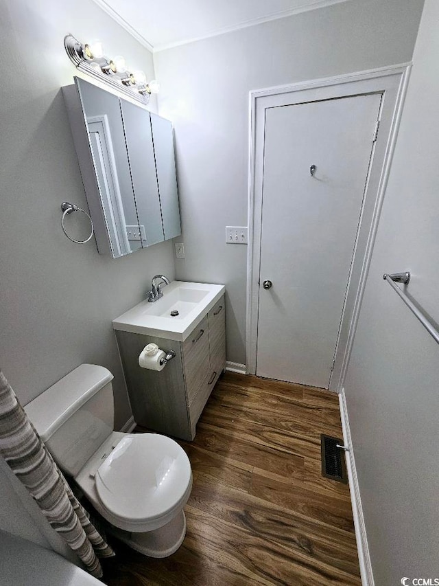 half bathroom with toilet, wood finished floors, vanity, visible vents, and ornamental molding