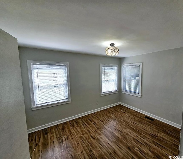 spare room with a wealth of natural light, visible vents, baseboards, and dark wood-style flooring