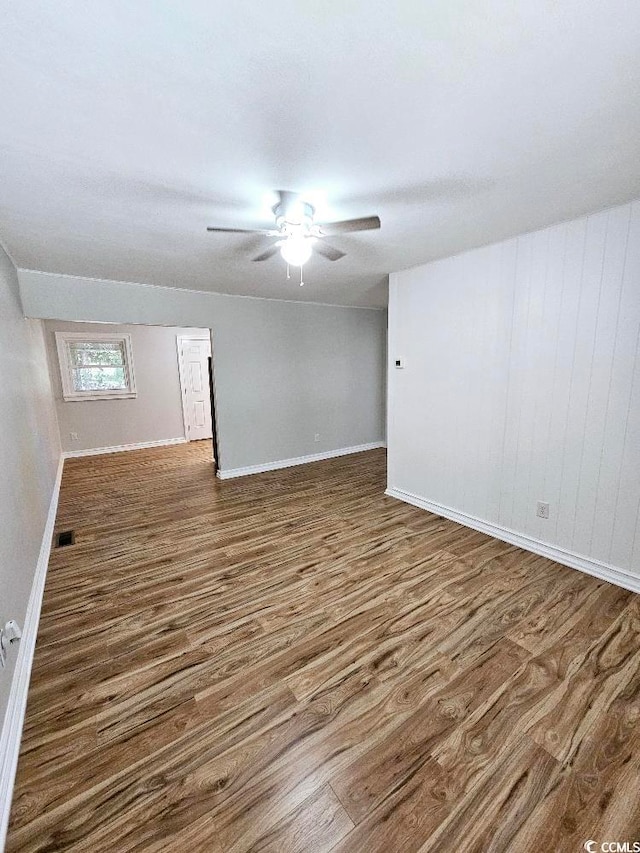 spare room with wood finished floors, a ceiling fan, and baseboards