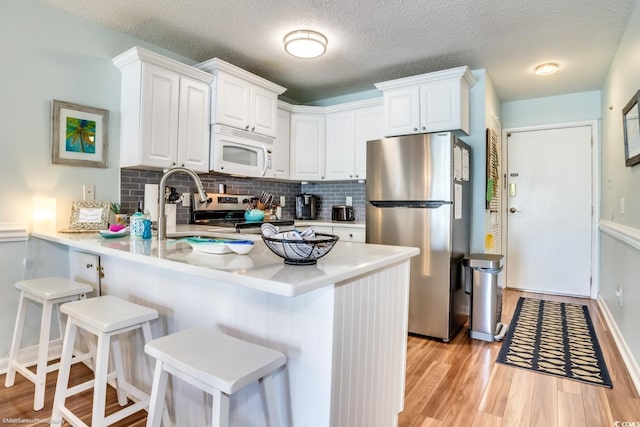 kitchen with a peninsula, light wood-style floors, stainless steel appliances, and light countertops