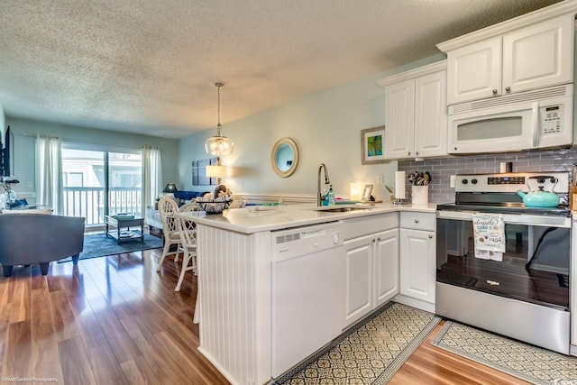 kitchen featuring light wood-style flooring, white cabinets, a sink, white appliances, and a peninsula