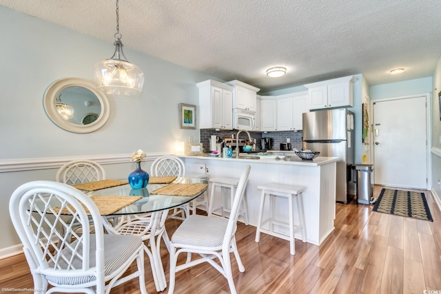 kitchen featuring freestanding refrigerator, a peninsula, light wood finished floors, and white microwave