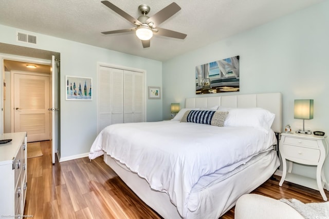 bedroom with a textured ceiling, wood finished floors, visible vents, baseboards, and a closet