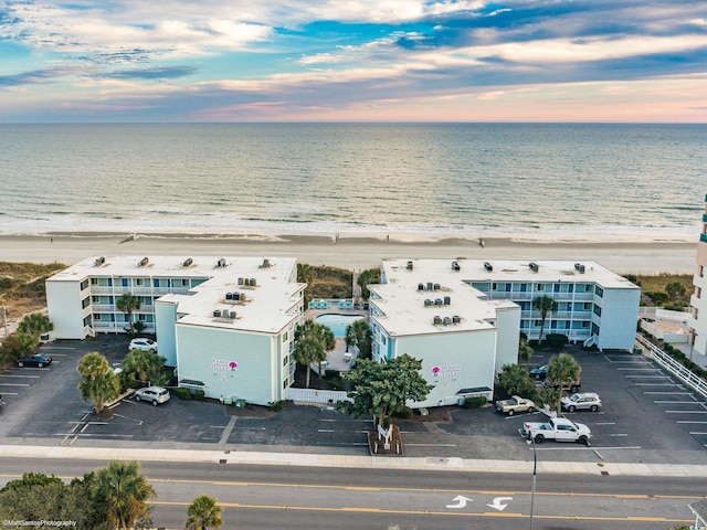 aerial view at dusk featuring a water view and a view of the beach