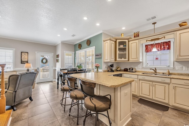 kitchen with visible vents, a breakfast bar area, a textured ceiling, cream cabinetry, and a sink