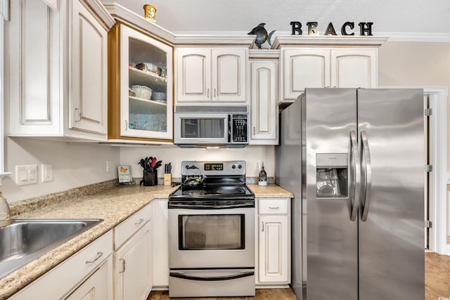 kitchen with glass insert cabinets, crown molding, appliances with stainless steel finishes, and a sink