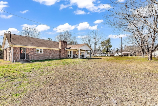 rear view of house with brick siding, a chimney, fence, and a lawn