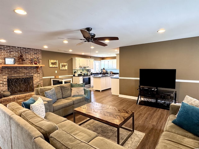 living area with dark wood-type flooring, a brick fireplace, a ceiling fan, and recessed lighting